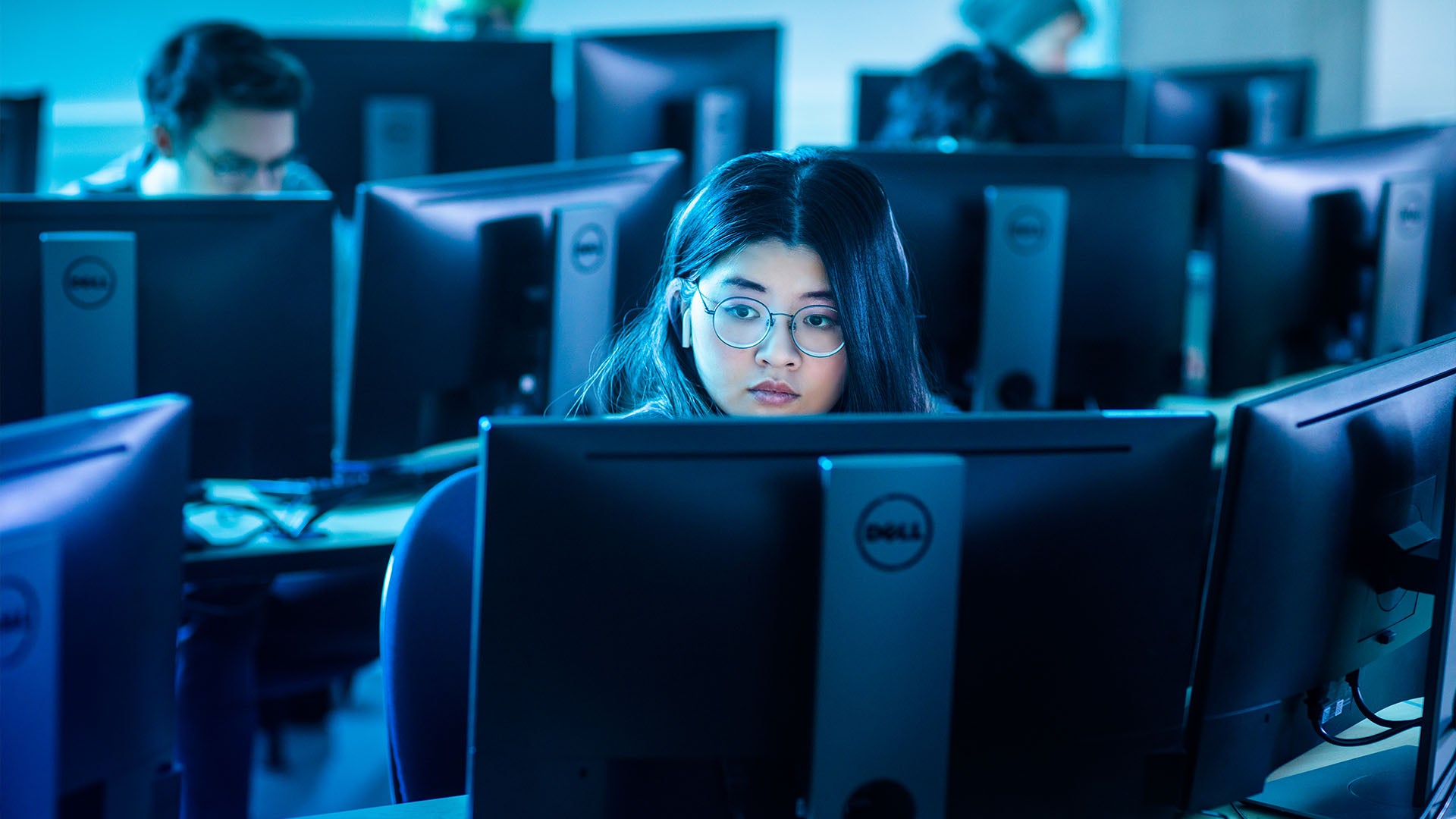 Female student wearing glasses sits in front of two dell computer monitors.