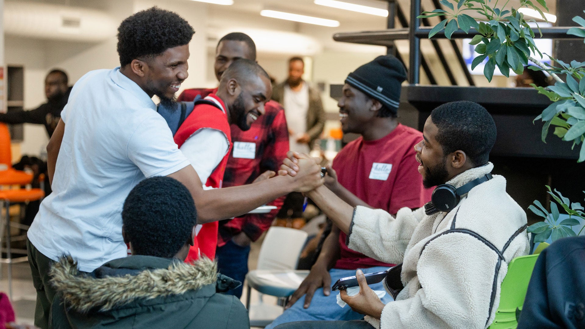 People gathered in a collaborative indoor workspace greeting each other with a handshake and conversation. People gathered in a collaborative indoor workspace greeting each other with a handshake and conversation.