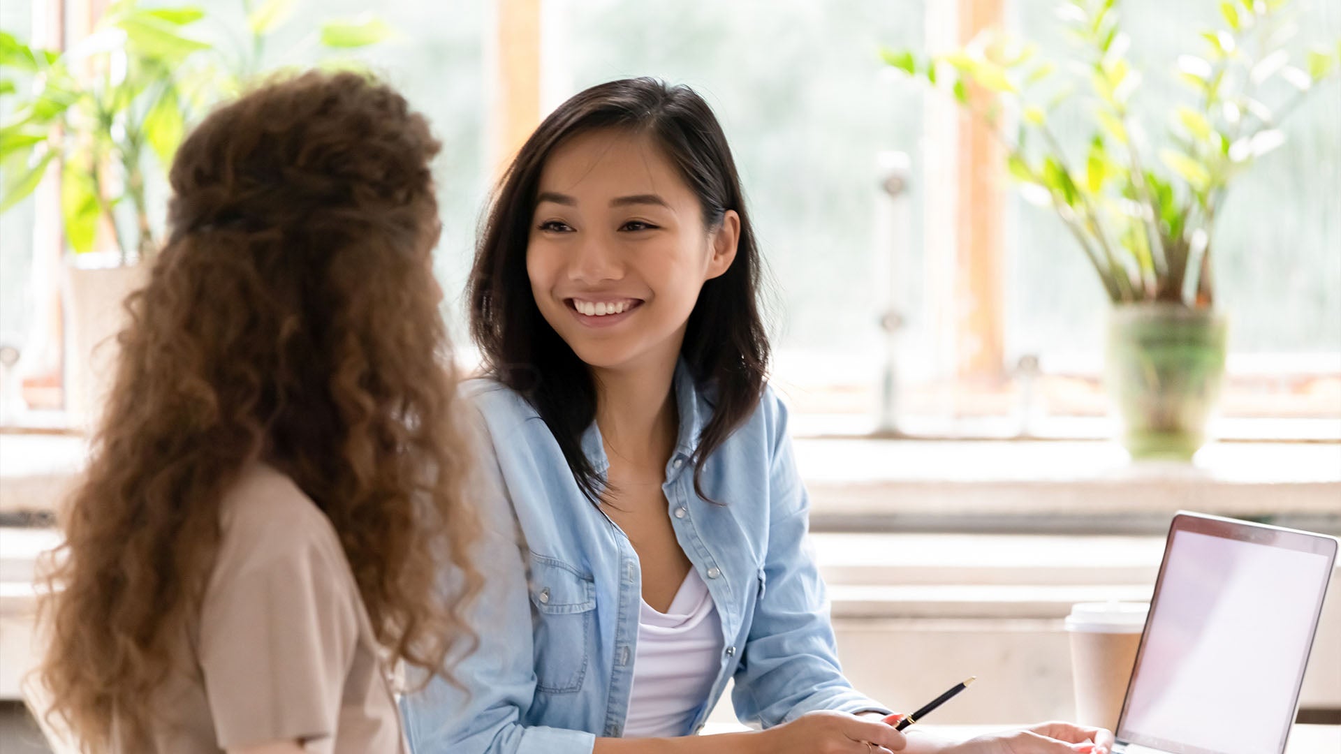 Two female human resources management students look at a tablet while smiling at each other.