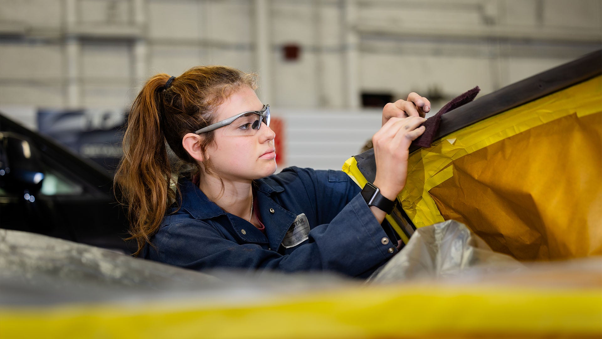 Female auto body technician student wearing safety glasses is sanding. Female auto body technician student wearing safety glasses is sanding.