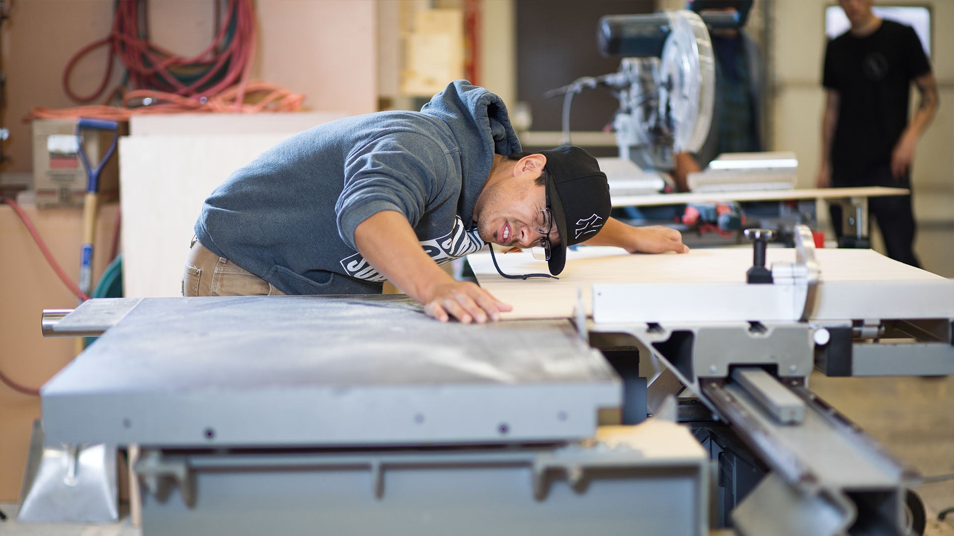 A man leaning forward, squinting at the cutting machine, with one hand holding the material and the other on the machine.