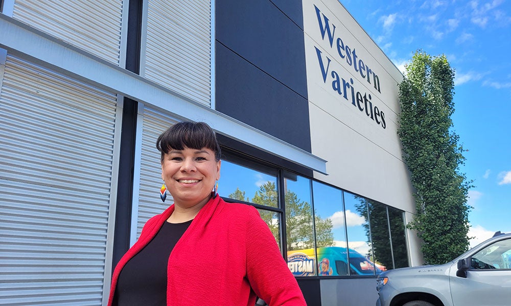 Woman standing outside the Western Varieties storefront, with the business sign visible above large windows and a parked vehicle nearby.