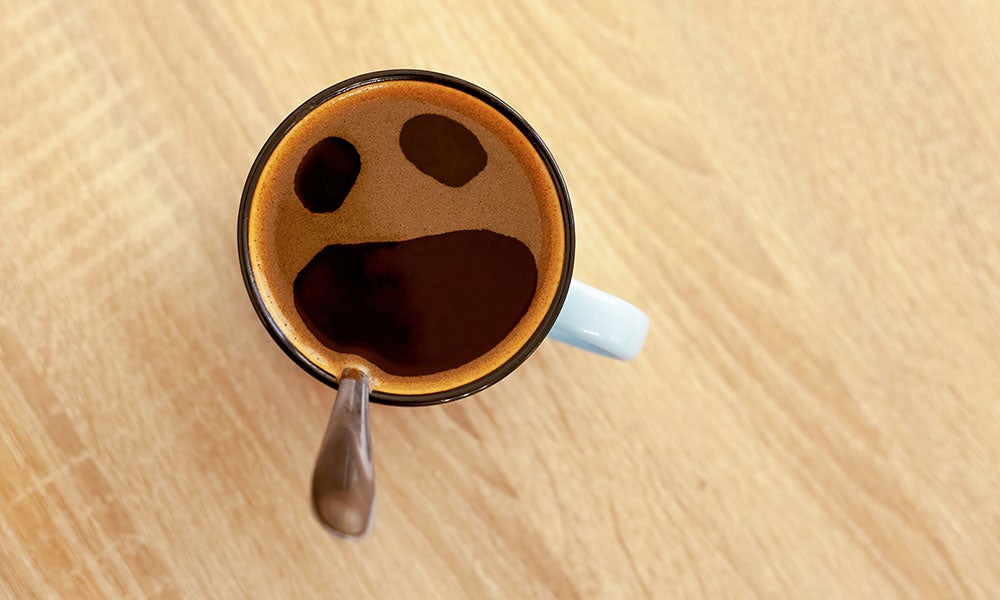 Top-down view of a coffee mug with foam and coffee creating a face-like pattern on a wooden tabletop.