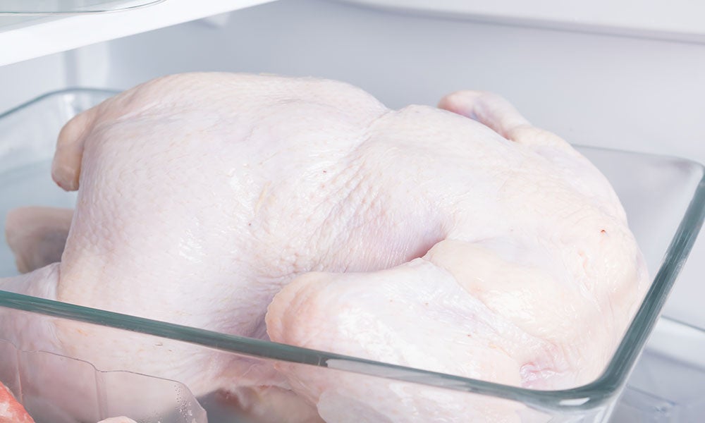 Raw turkey stored in a glass baking dish on a refrigerator shelf.