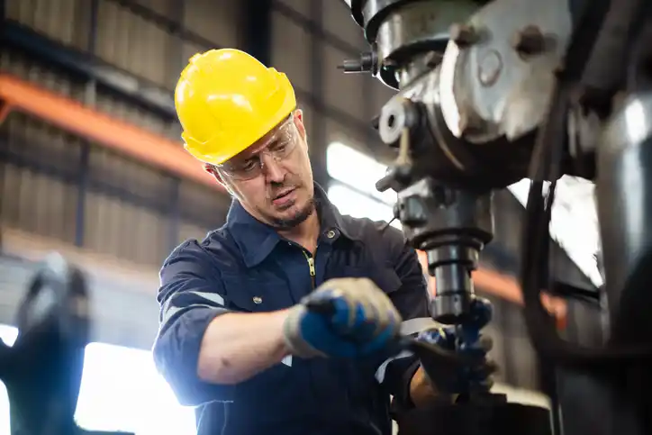 A mechanic working wearing a yellow helmet and blue overalls.