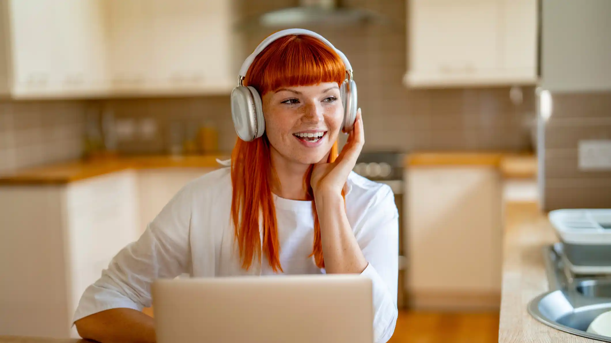 Cheerful Woman Enjoying Music While Working on Her Laptop in a Bright Kitchen