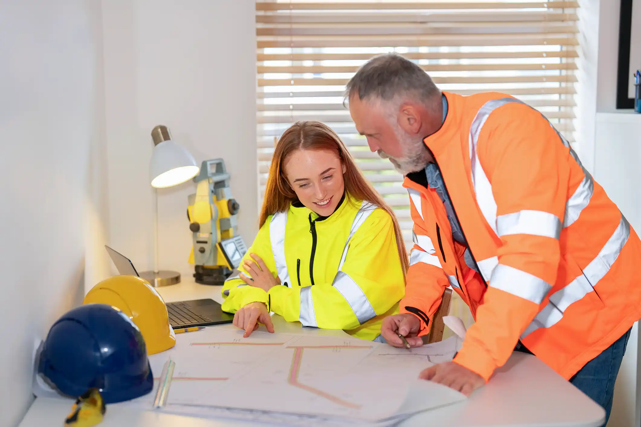 Collaborative planning session between two professionals in bright safety gear in a modern office