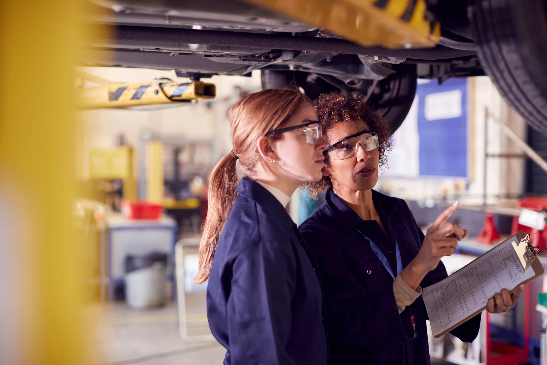 Apprentice with employer wearing protective wear in an automotive engineering lab