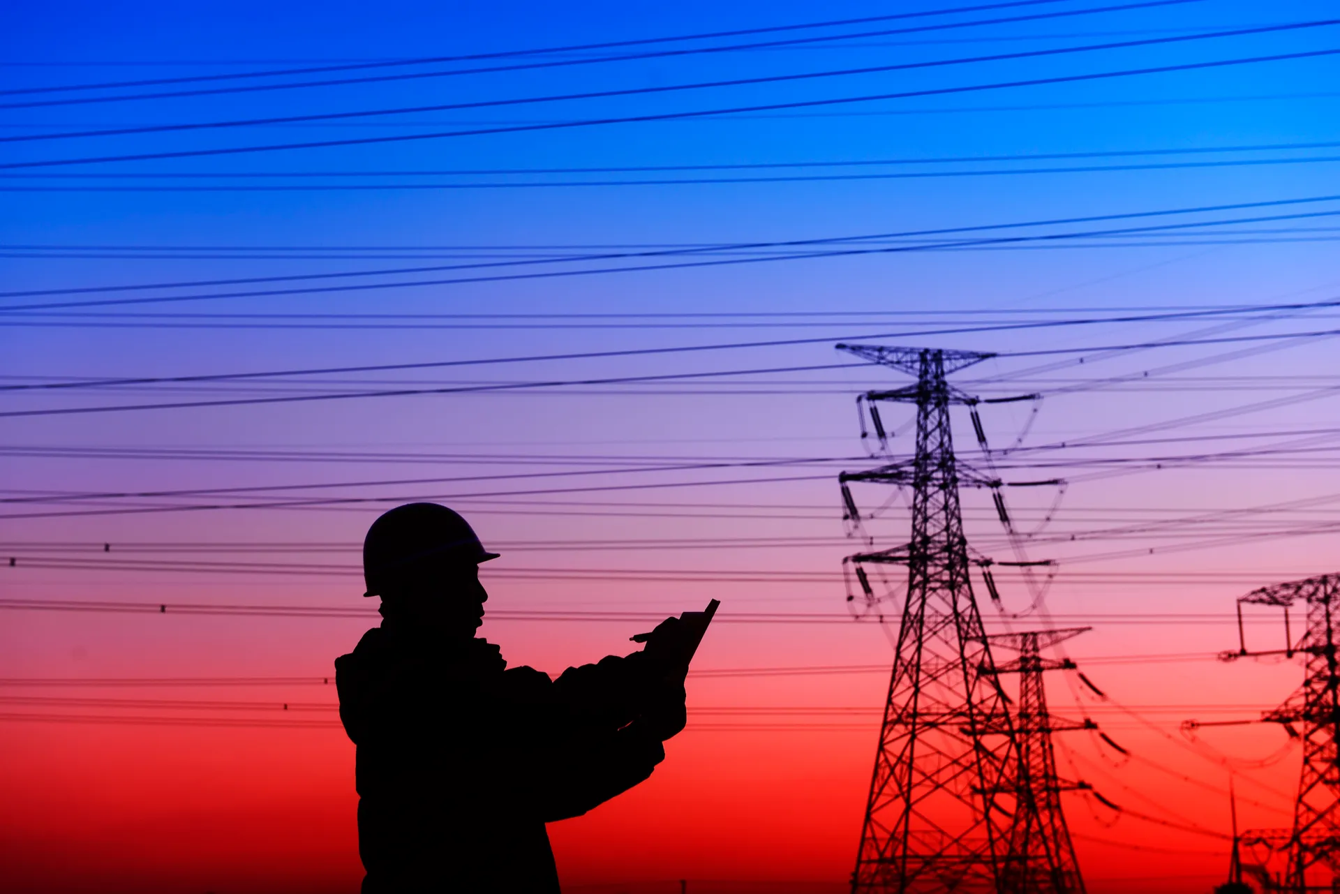 Worker and electricity tower silhouette against sunset