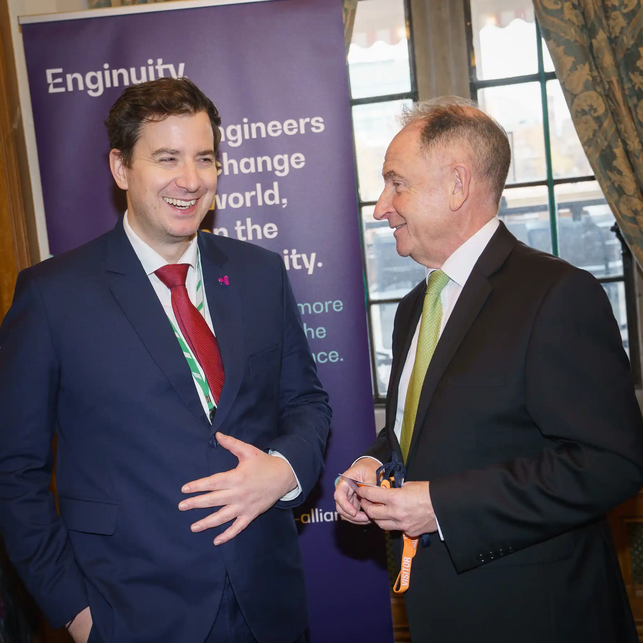 Two attendees at the Enginuity Alliance launch event talking and smiling in front of a branded banner