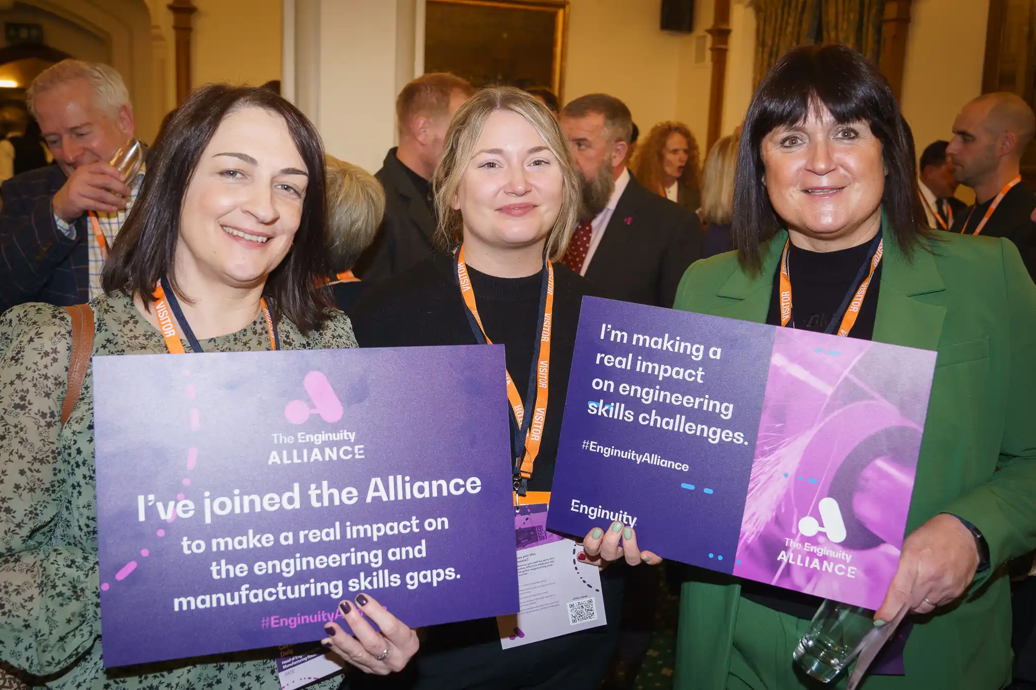 Three attendees holding up signs about their support at the Enginuity Alliance launch event