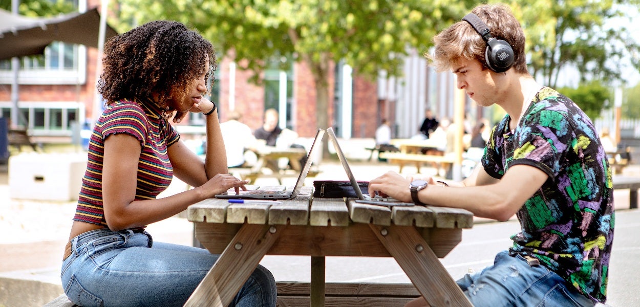 Een man en vrouw zitten aan een picknicktafel gefocust achter hun laptop.