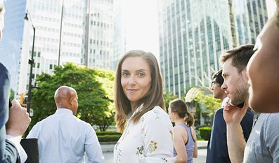 Groepje mensen, een vrouw kijkt in de camera, op de achtergrond hoge kantoorgebouwen