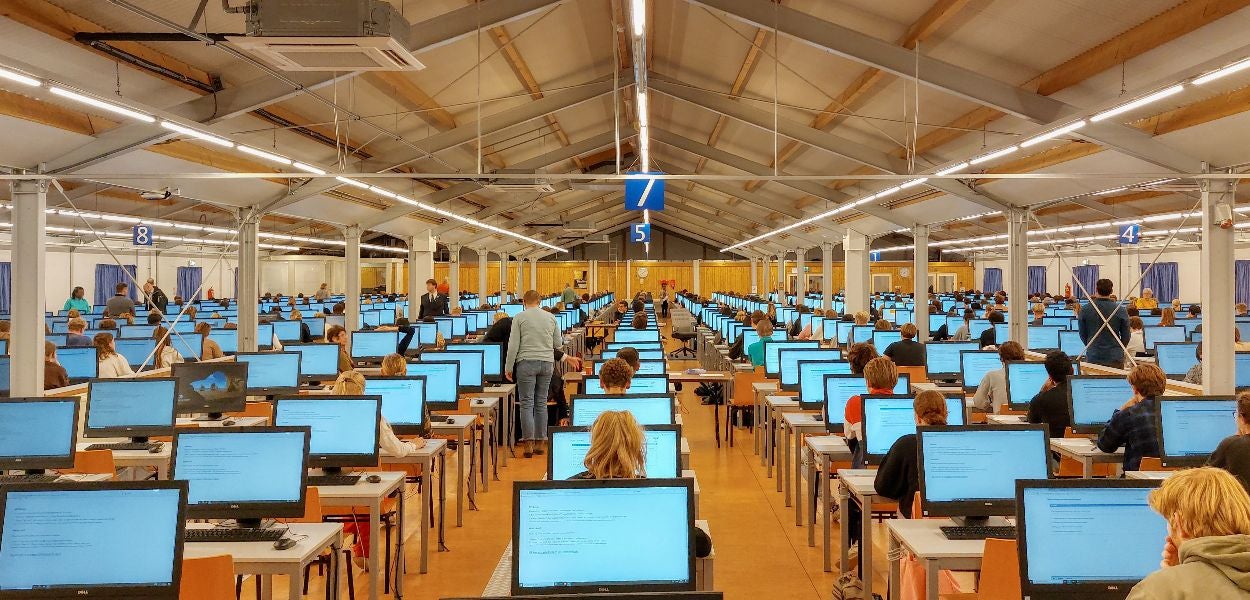 Een grote tent vol studenten die achter computerschermen bezig zijn met een digitale toets.