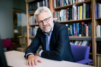 Een man aan een tafel met een boekenplank achter hem