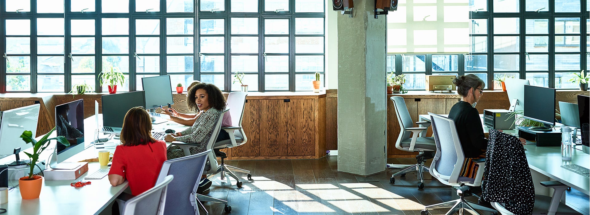 Two women are talking to each other and another colleague is working behind a computer