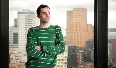 Student staat binnen voor een raam, op de achtergrond de Zuidas