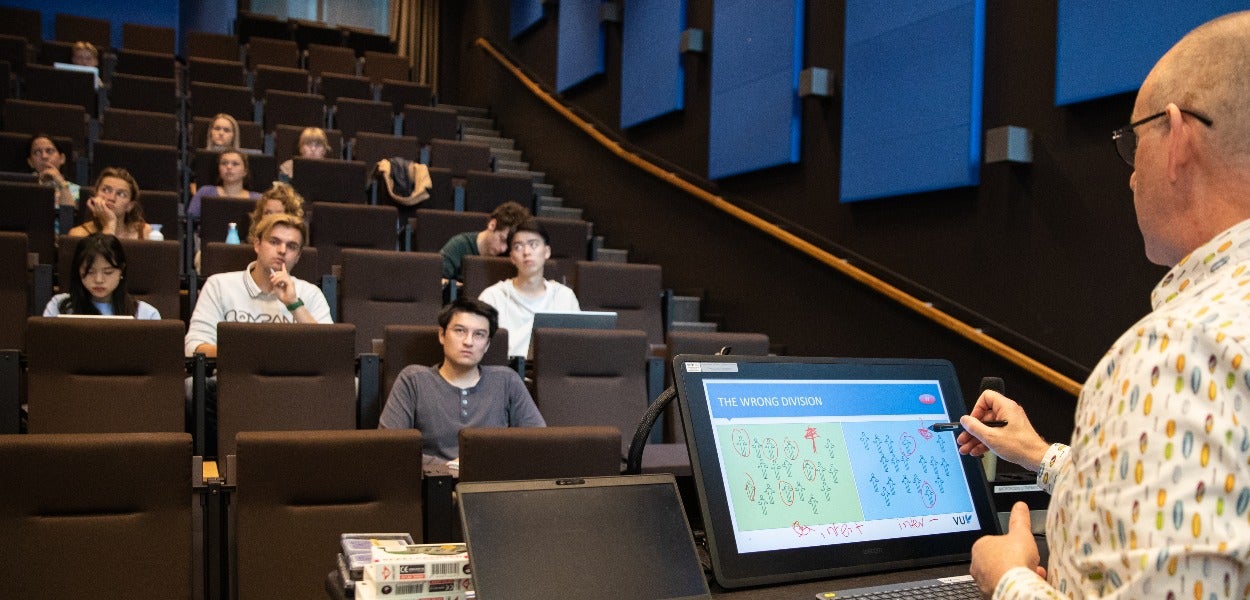 A teacher during class in a lecture hall while students listen to him. 