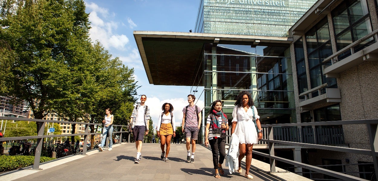 Studenten lopen uit het VU-hoofdgebouw op een zonnige dag.