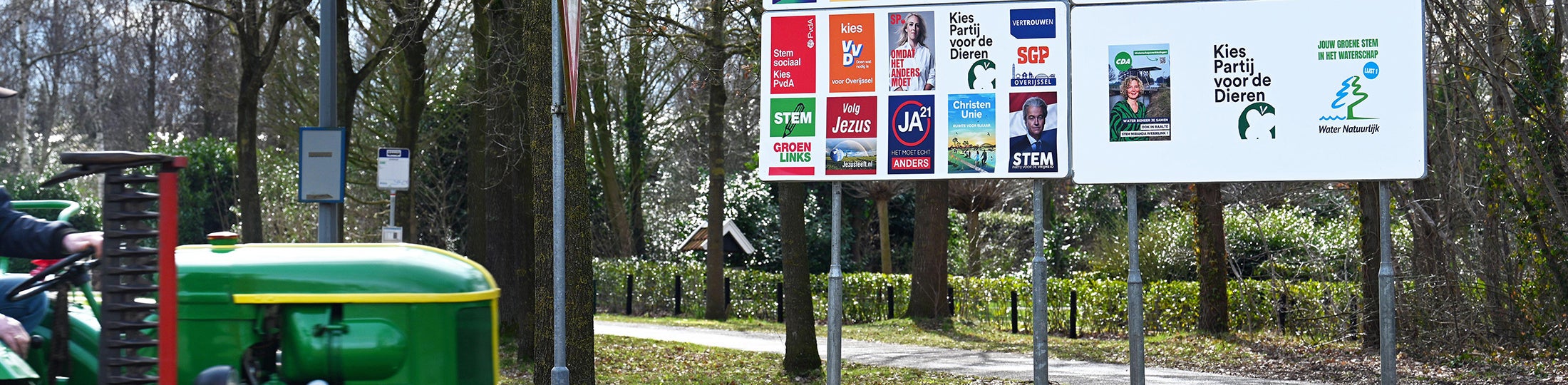 Tractor rijdt langs buitenreclamebord met verschillende verkiezingsposters