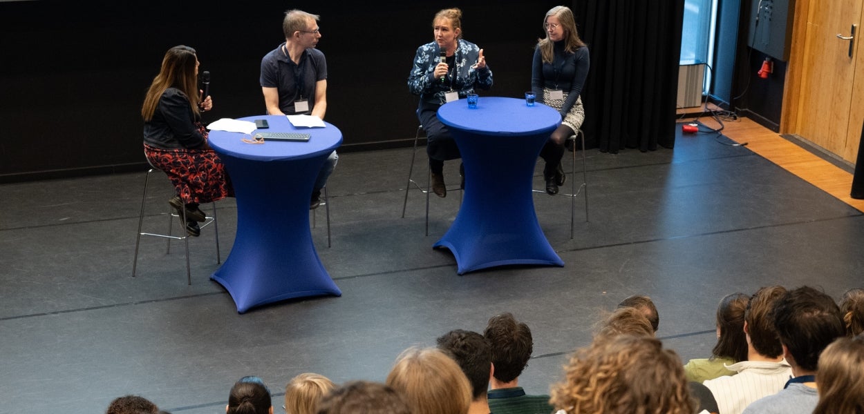 Four people at high tables on a stage during a panel discussion with audience