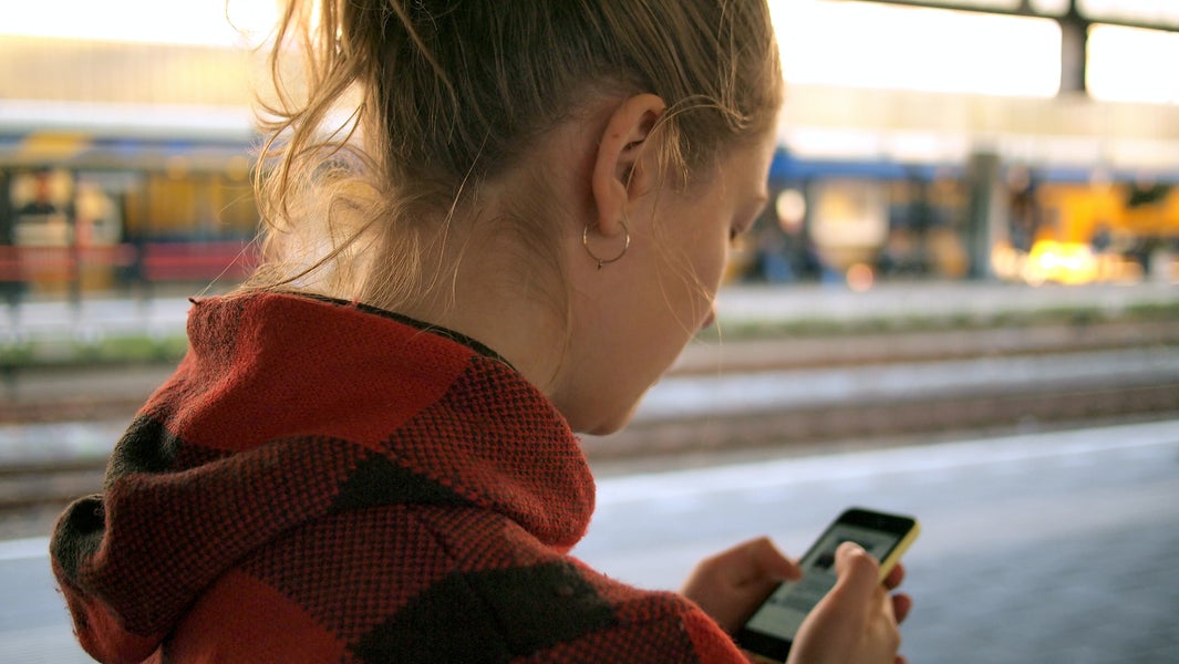 Een vrouw kijkt op haar telefoon op het perron.