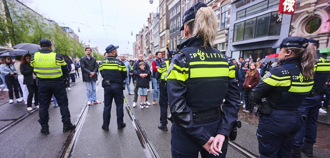 Nederlandse politieagenten in uniform op de rug gezien op een straat met tramrails tegenover een groep mensen