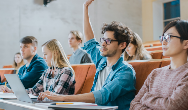 Een student steekt zijn hand op in een collegezaal