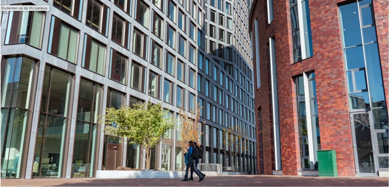 Two students walk past a modern university building with large glass windows.