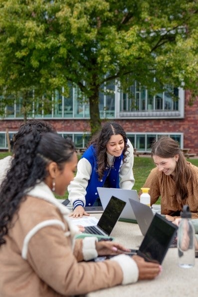 Een groep studenten met laptops buiten aan een tafel