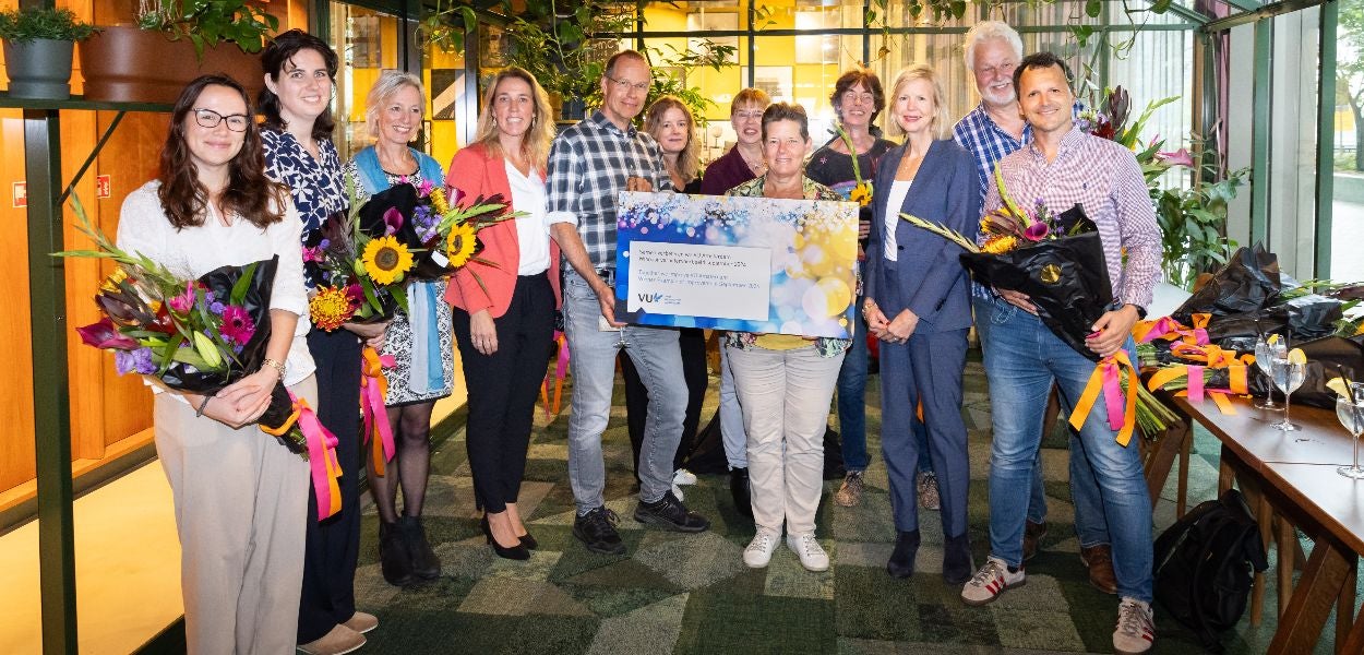 Group photo of people holding flowers and a large certificate. 