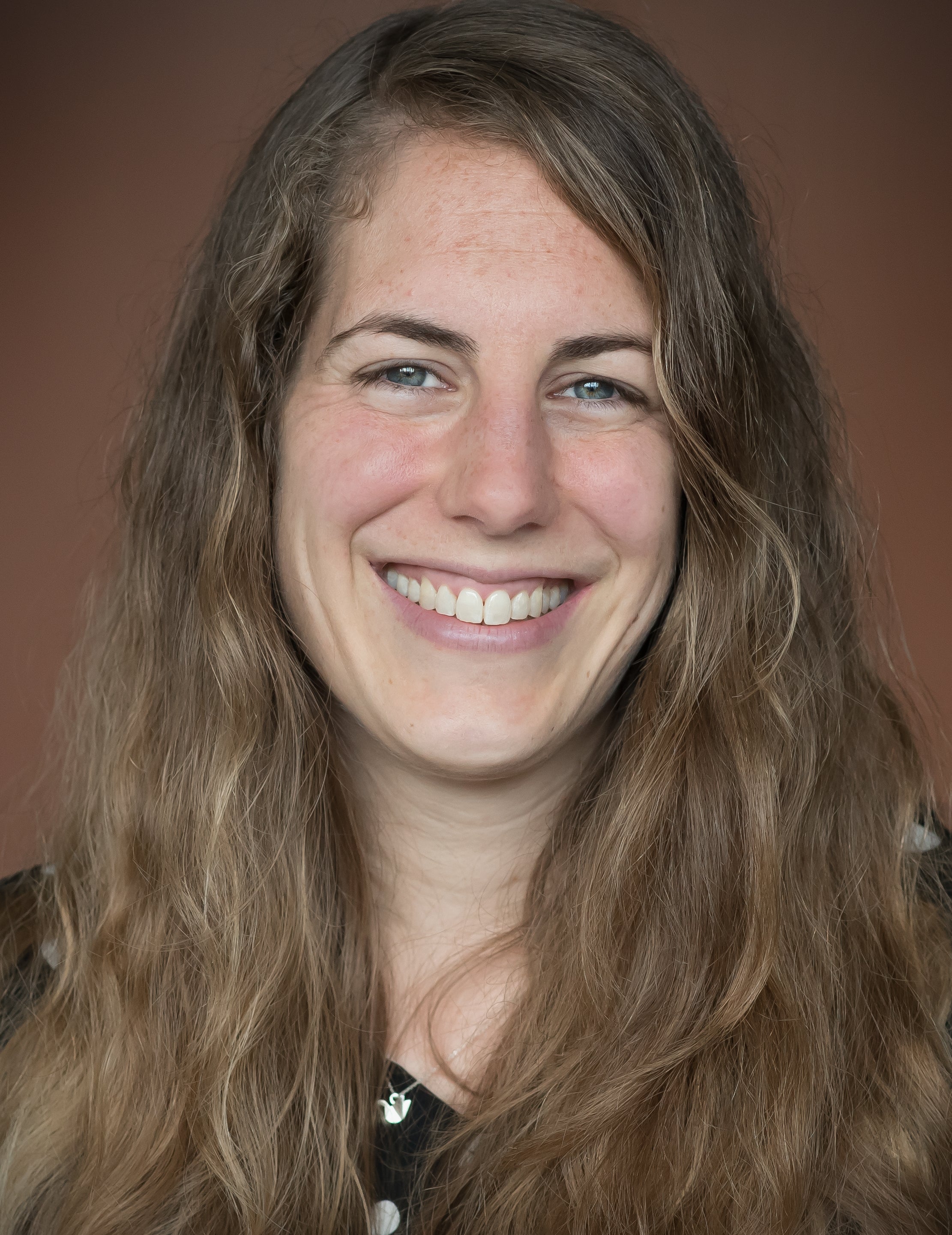 Headshot of a smiling young woman with long wavy mid-blond hair