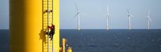 Bouwvakker klimt op windturbine op zee. Andere windmolens staan op de achtergrond. 