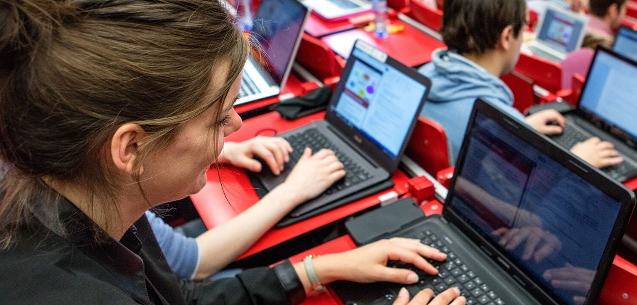 A woman with brown hair uses her laptop in a lecture hall.