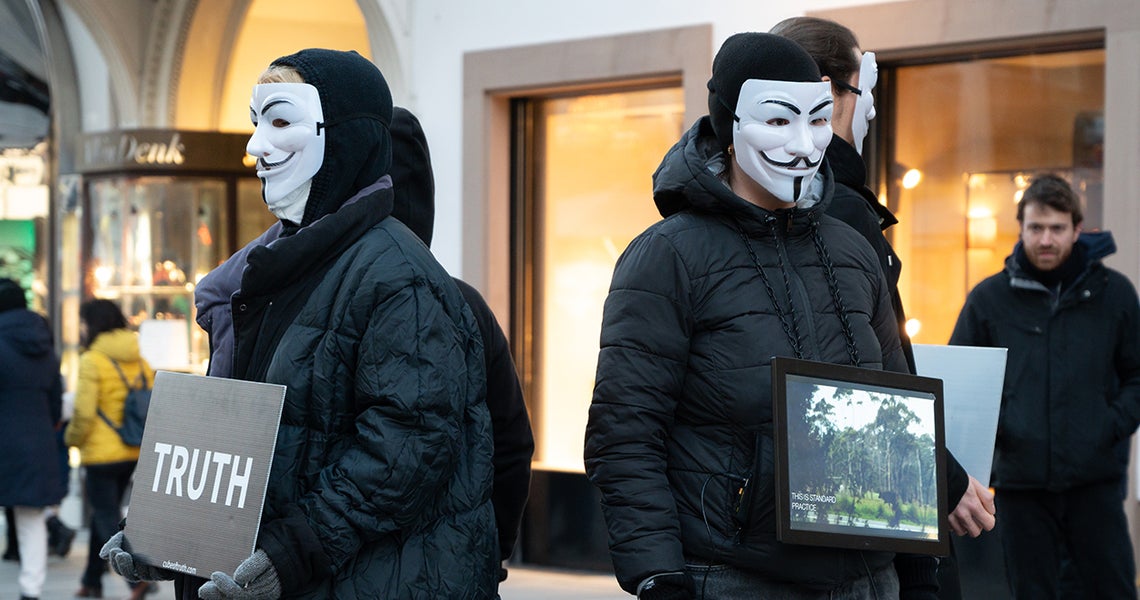Protestors with white masks hold signs of truth