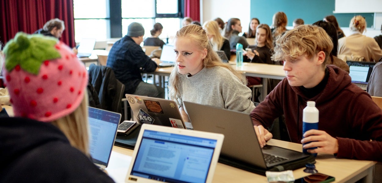 Students working focused on their laptops in a classroom.