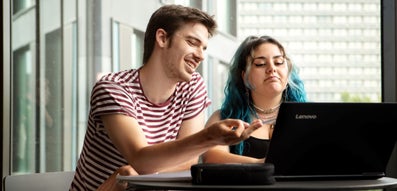 Two students look at a laptop while one points to something on the screen