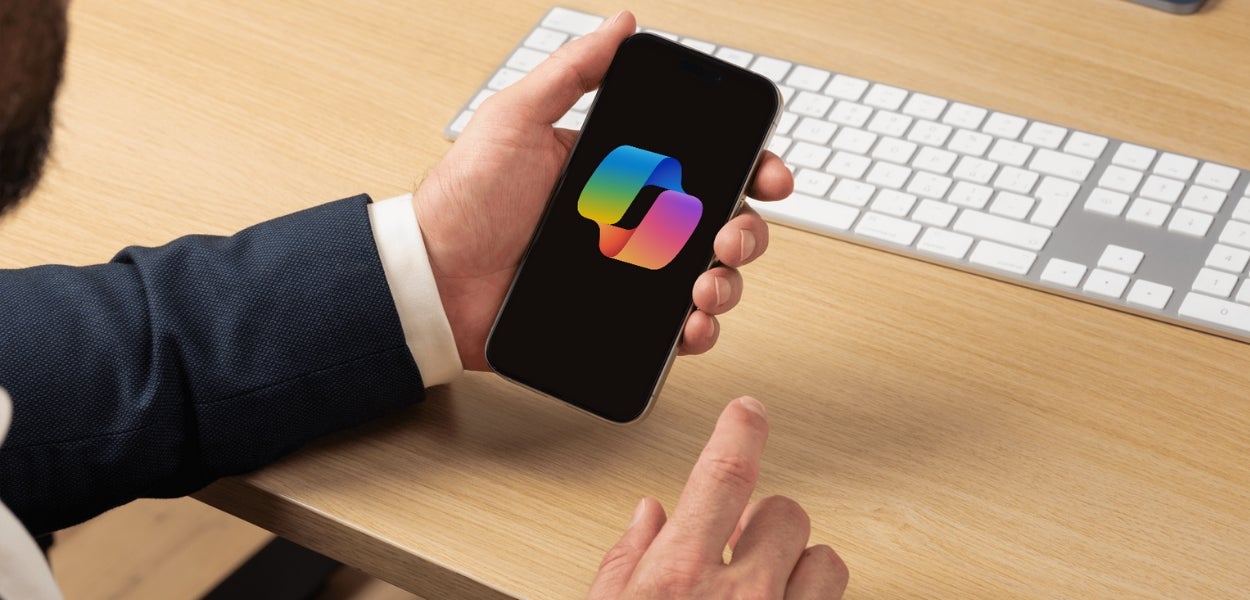 A man holds a phone showing MS Copilot's logo.