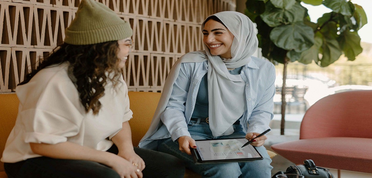 Vrouw met hoofddoek en vrouw met muts lachen naar elkaar