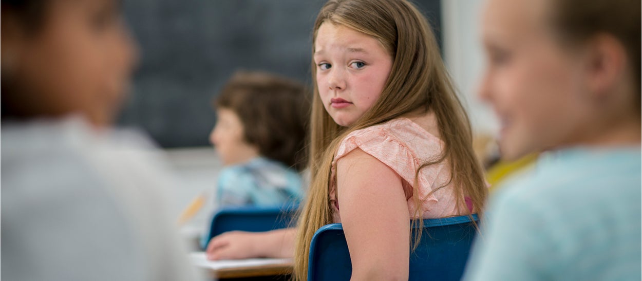 Meisje in schoolklas kijkt achterom naar twee kinderen die over haar praten