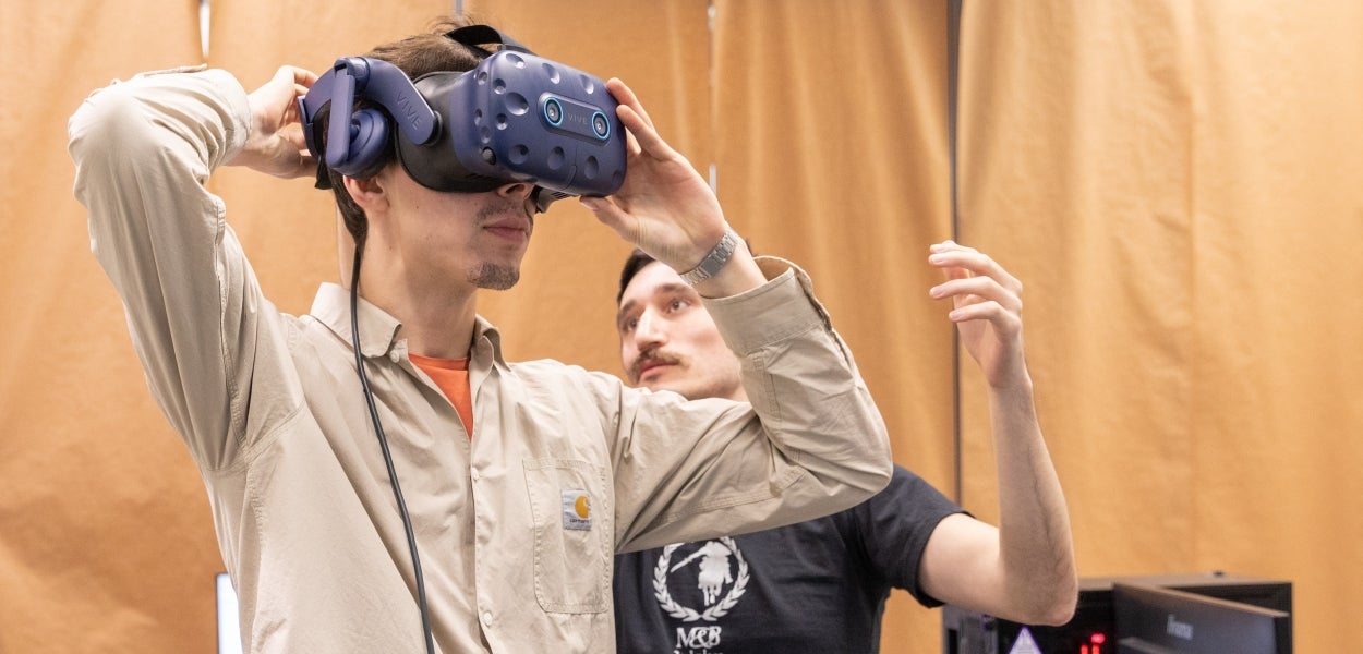 Een man heeft een VR-headset op en wordt geassisteerd door een andere man.