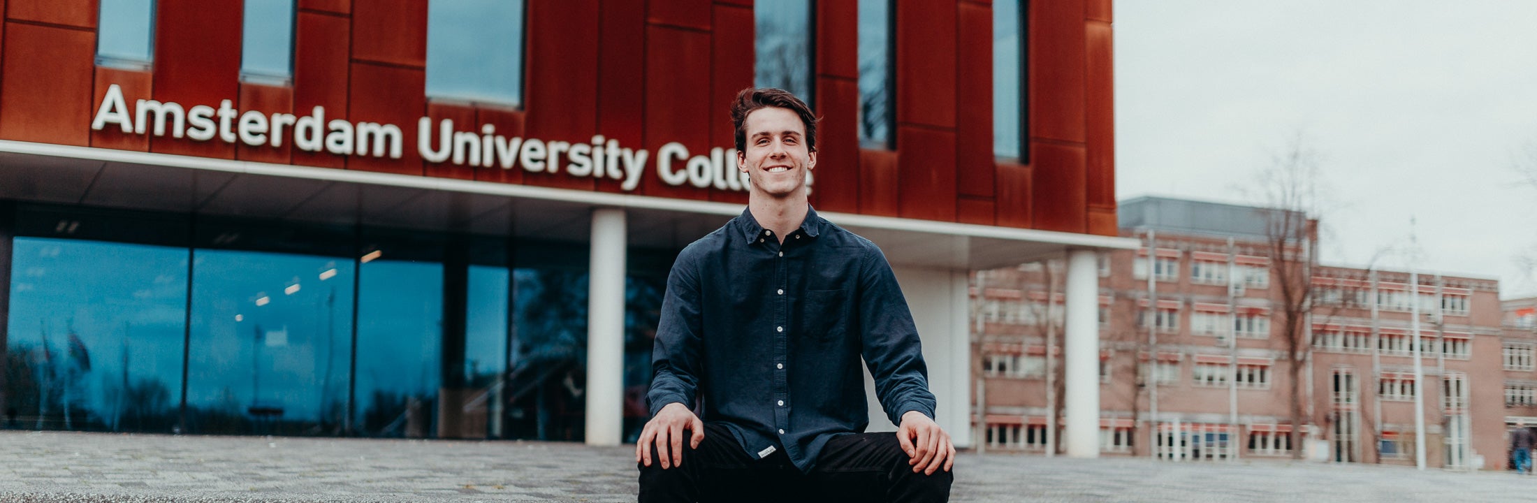 Student sitting in front of the entrance of Amsterdam University College