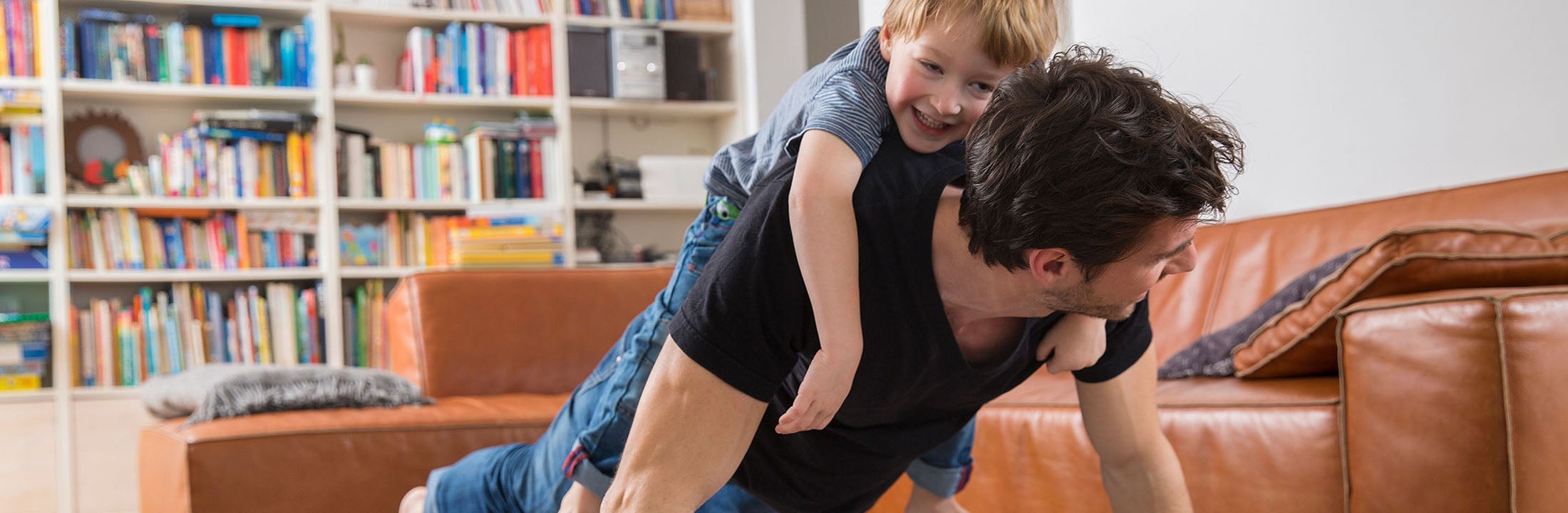 Little boy hanging on the back of a crawling man, laughing