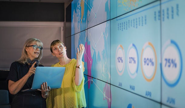 Two women discuss figures on the big screen