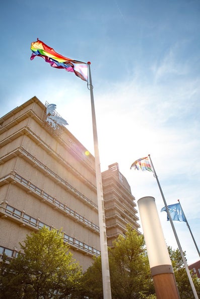 Pride flag fluttering in the wind atop a flagpole in front of the main building of Vrije Universiteit Amsterdam