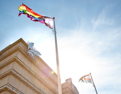 Pride flag fluttering in the wind atop a flagpole in front of the main building of Vrije Universiteit Amsterdam