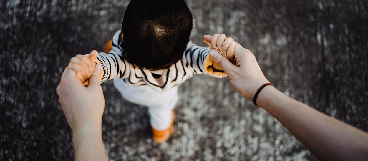A baby is taking his first steps while someone is holding its hands 
