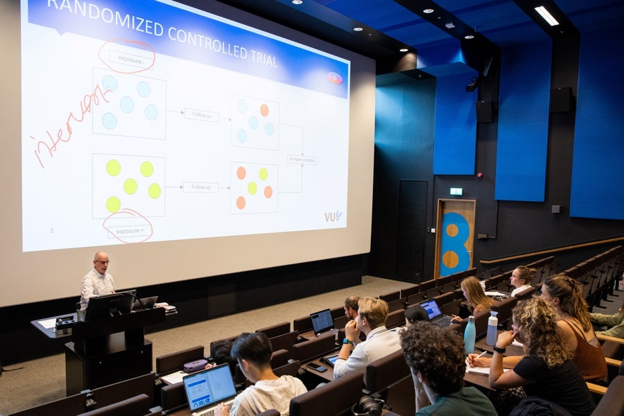 Docent voor een groot projectiescherm in een collegezaal vol studenten