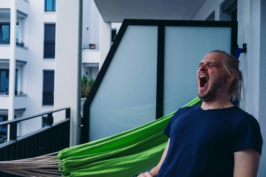 Een man zit op zijn balkon en gaapt