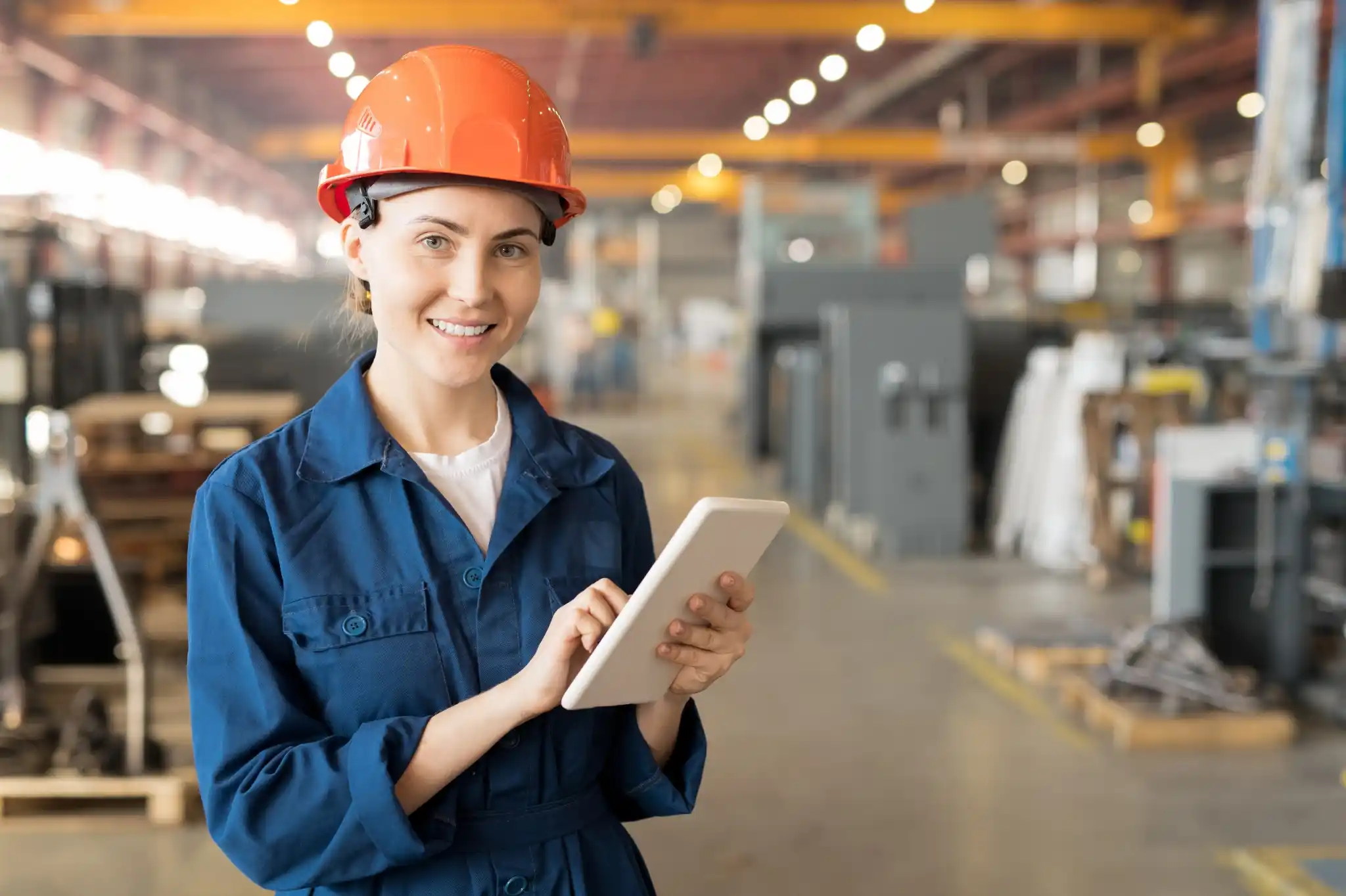 Woman engineer in blue coat and orange helmet in a factory